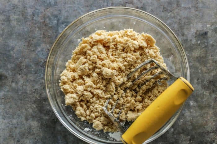 making crumble topping in a clear bowl, with a rigid pastry cutter