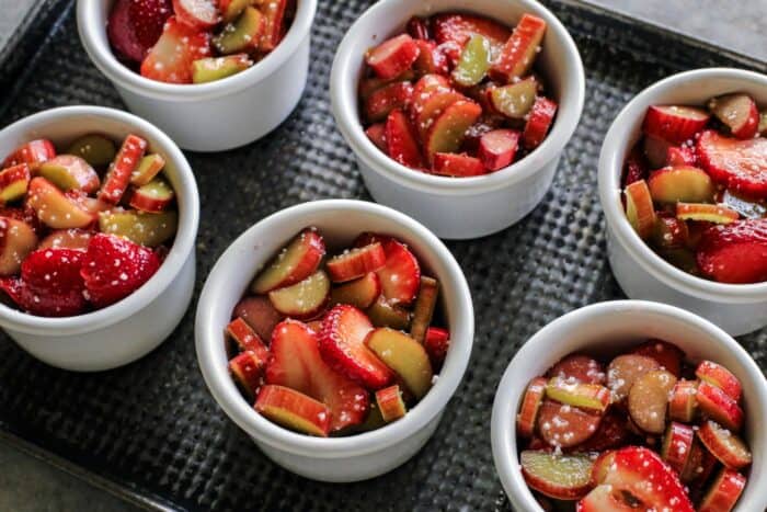 sliced strawberries and rhubarb in ramekins on a metal pan