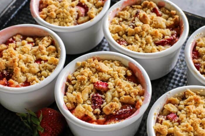 ramekins on a pan, filled with a baked crumble that includes rhubarb and strawberries