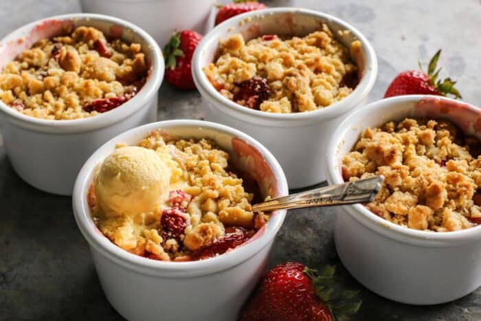 ramekins of rhubarb and strawberry crumble, one with a scoop of melty vanilla ice cream