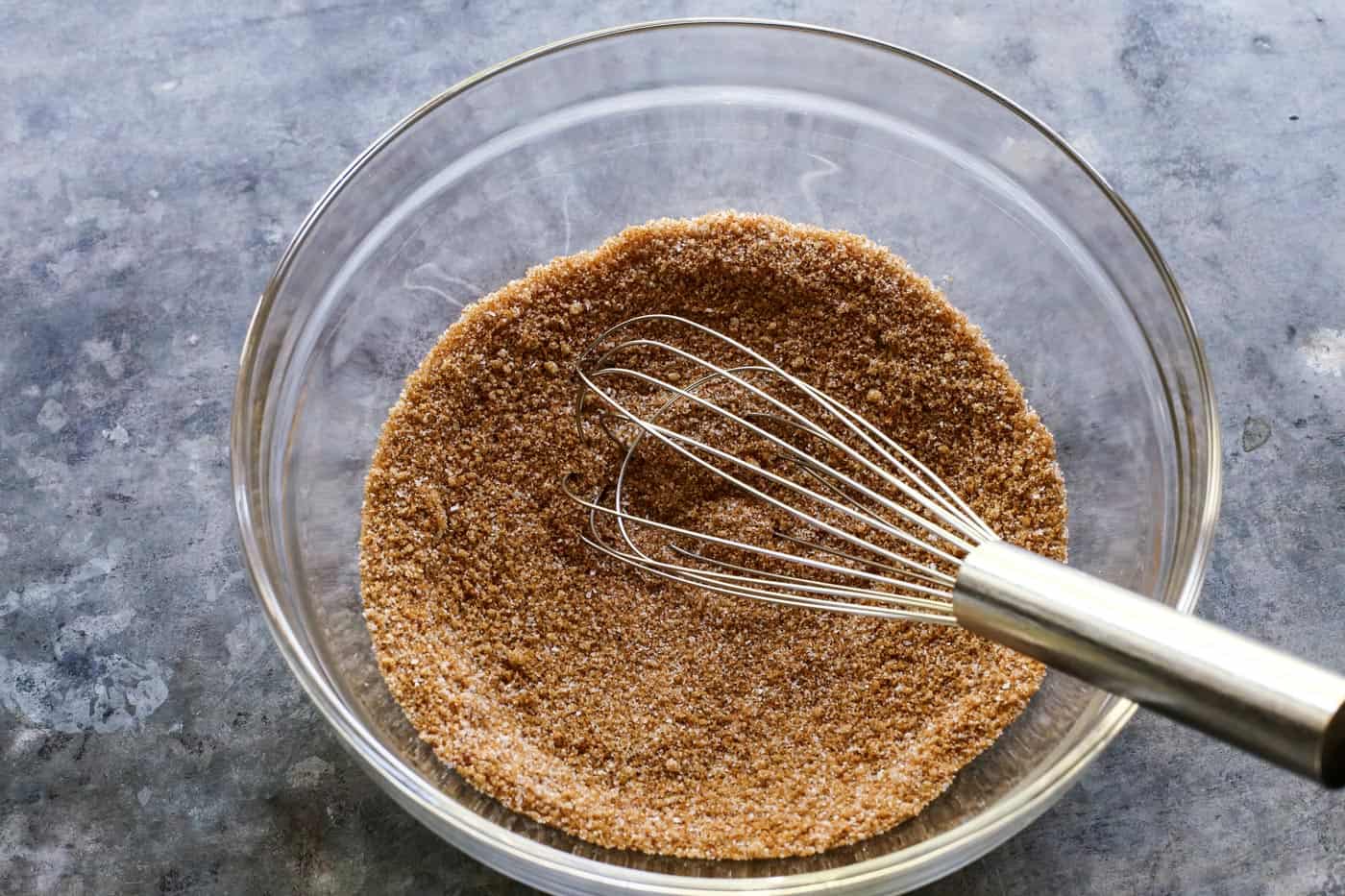 whisk and clear bowl with a mixture of sugars, salt, cayenne, and cinnamon