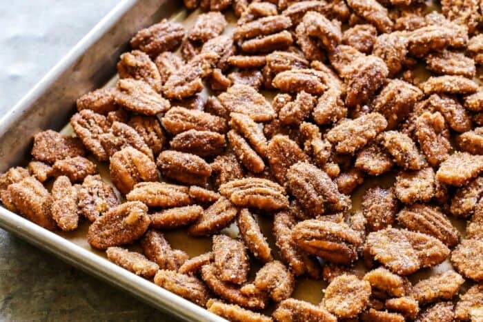 sugar-coated pecans spread out on a rimmed baking pan