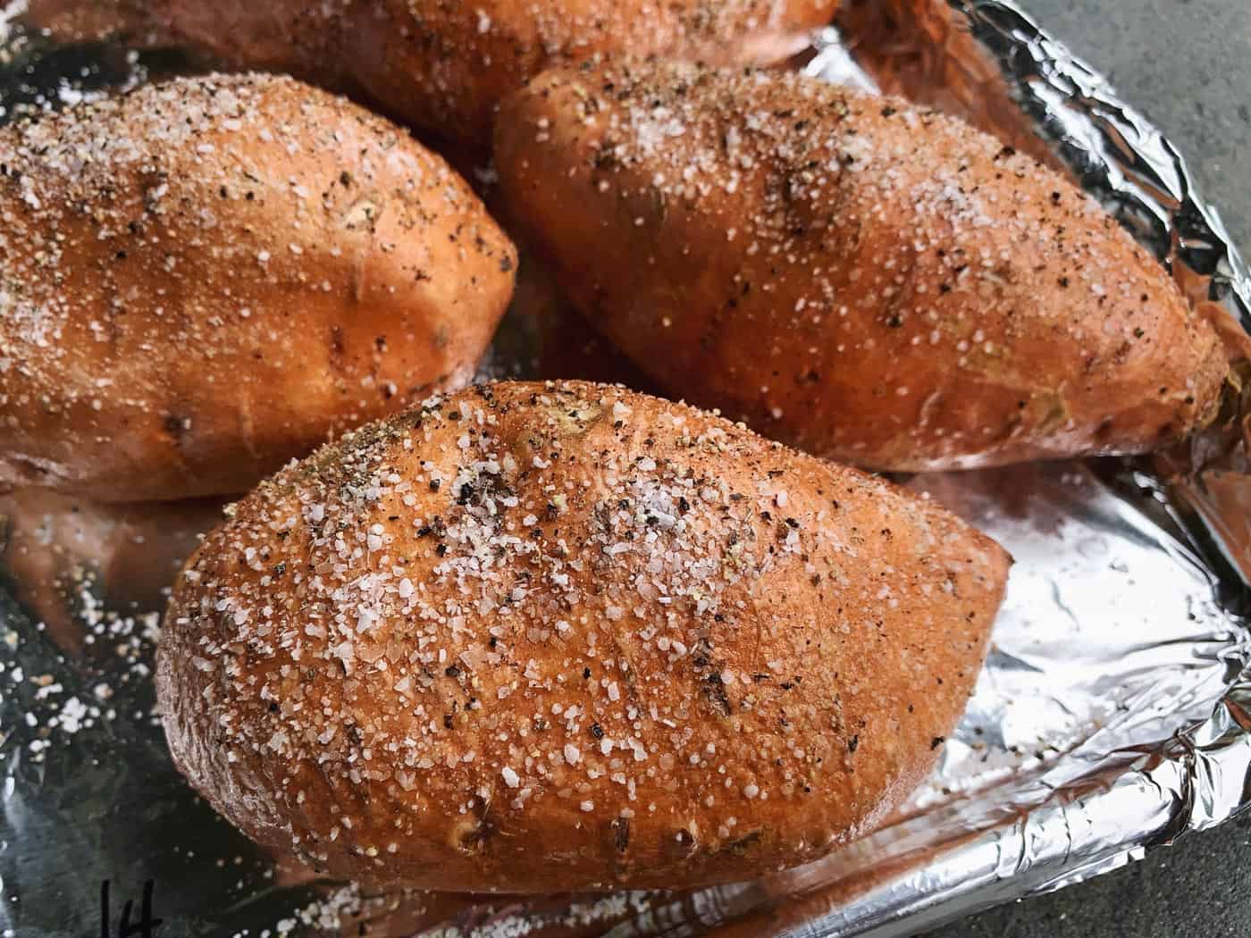 sweet potatoes seasoned with salt and pepper, on a foil-lined pan