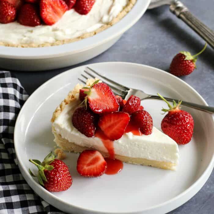 a slice of cream cheese pie with strawberry topping, on a white plate