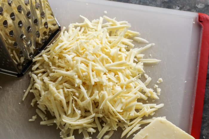 a box grater and block of Monterey Jack cheese getting shredded