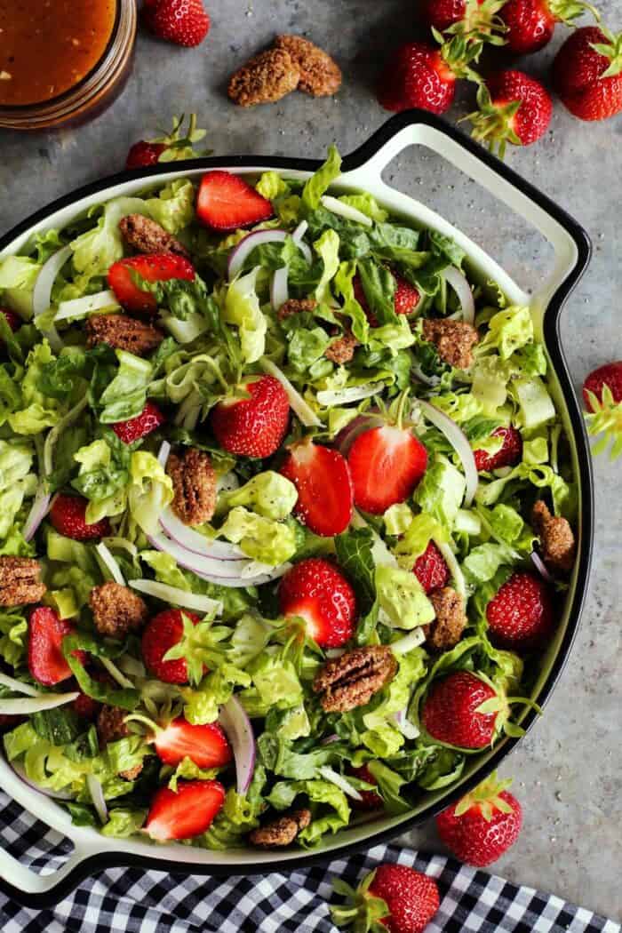 romaine salad with fresh strawberries and candied pecans, in a large white bowl