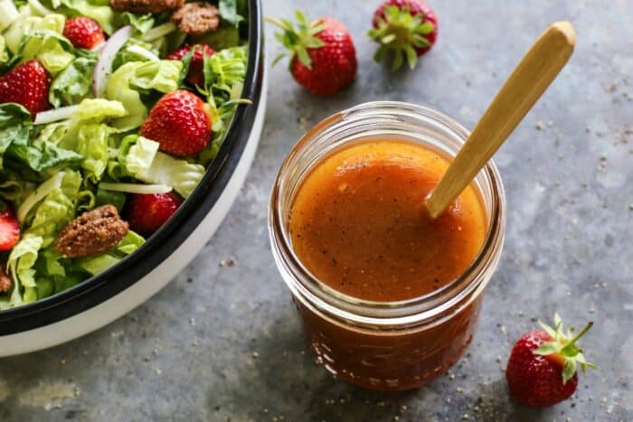 jar of dressing and a bowl of lettuce salad with strawberries