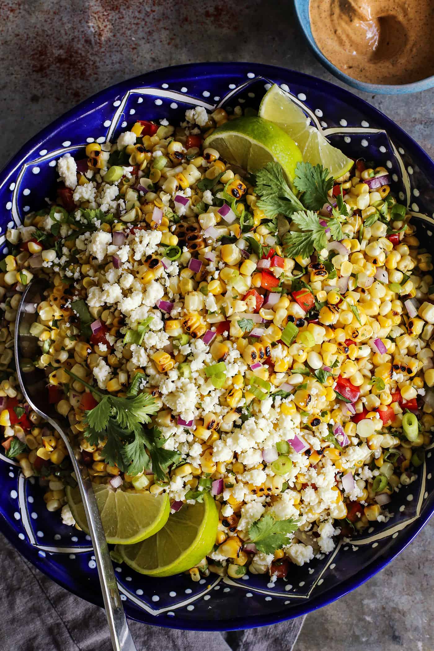 This Mexican Corn Salad, known as esquites, features grilled corn, a tangy, creamy dressing, and plenty of spice. Mexican corn salad in a dark blue pottery bowl