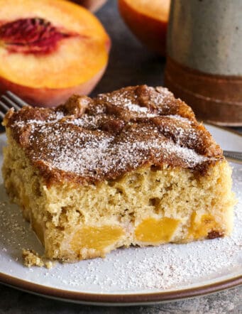 a piece of peach cake on a plate, plus a fresh sliced peach