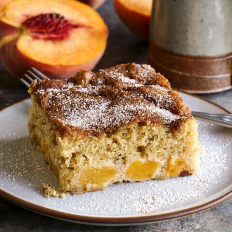 a piece of peach cake on a plate, plus a fresh sliced peach