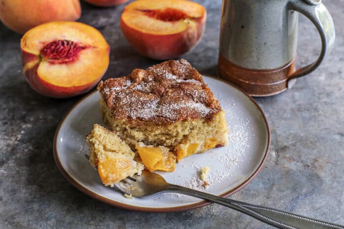 a forkful of peach cake on a plate with a piece of cake