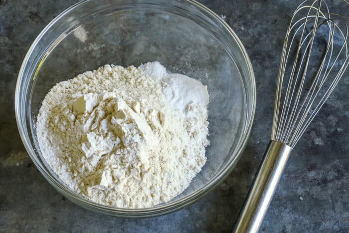 a clear mixing bowl with flour, baking soda, and salt, plus a whisk