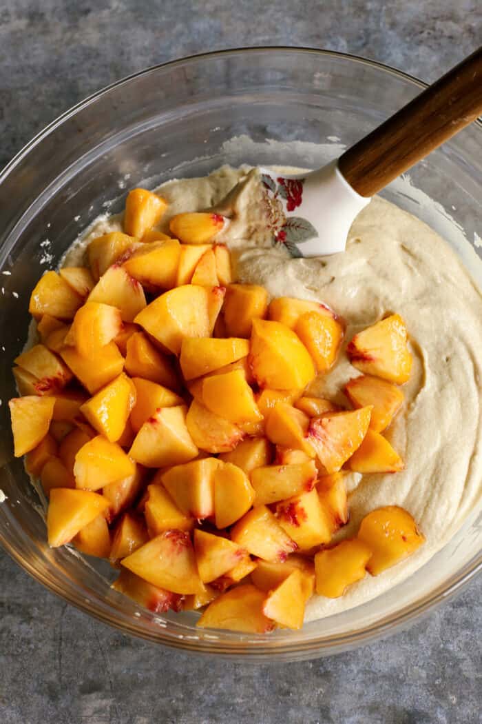 a clear bowl of cake batter topped with fresh sliced peaches