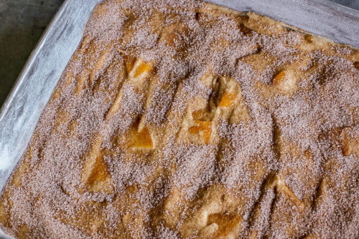 peach cake batter in a metal pan, topped with cinnamon sugar mixture