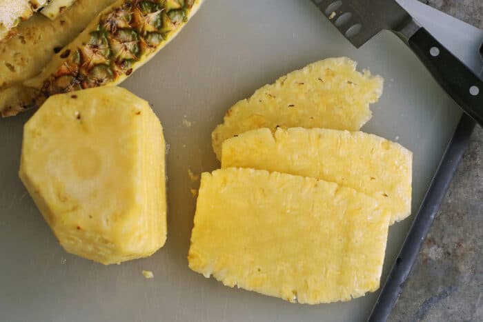 slices of pineapple on a cutting board, with a large knife