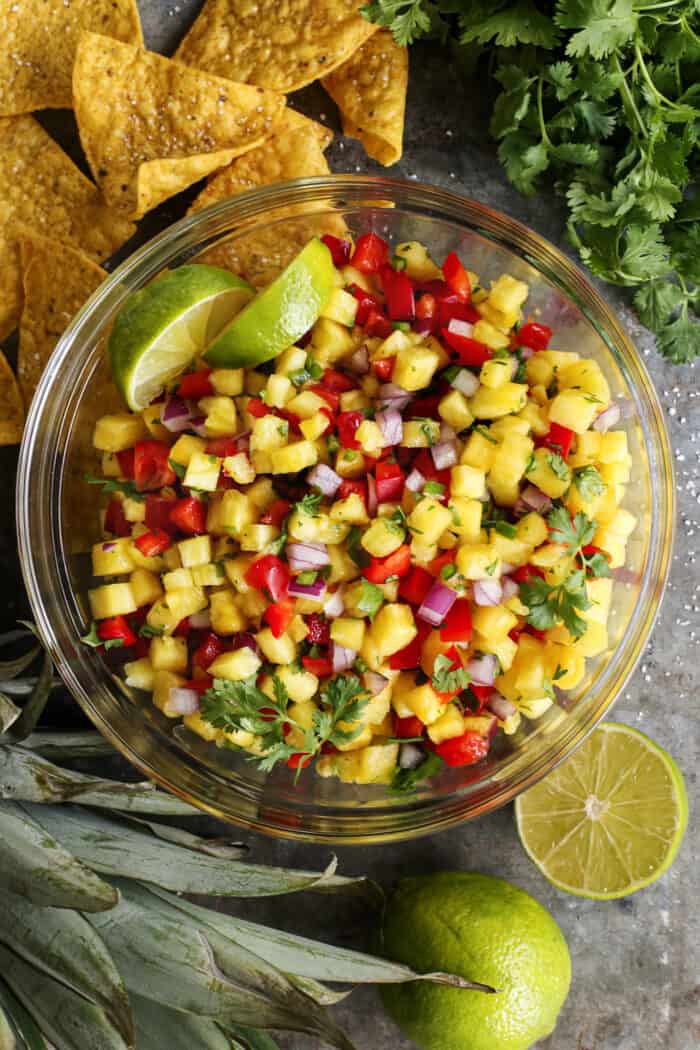 large clear bowl of pineapple salsa, plus tortilla chips and limes