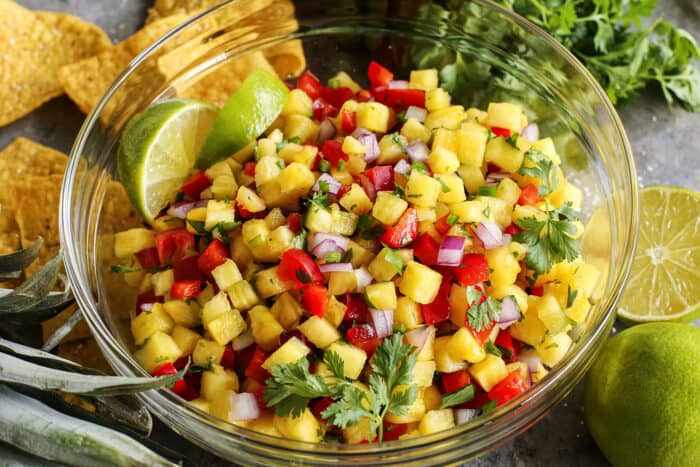 a large clear bowl of homemade pineapple salsa, plus chips and limes