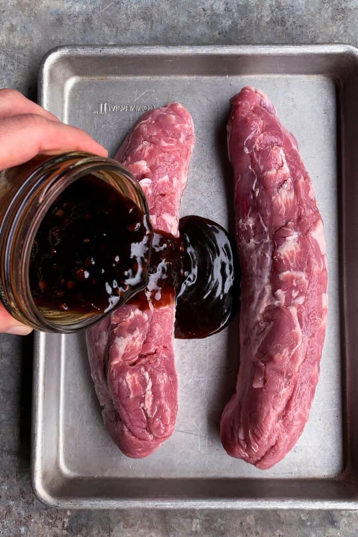 pouring teriyaki sauce over pork tenderloin on a rimmed pan