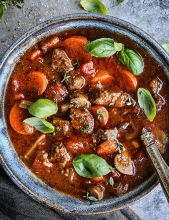 a blue pottery bowl with Italian beef soup, garnished with fresh basil leaves