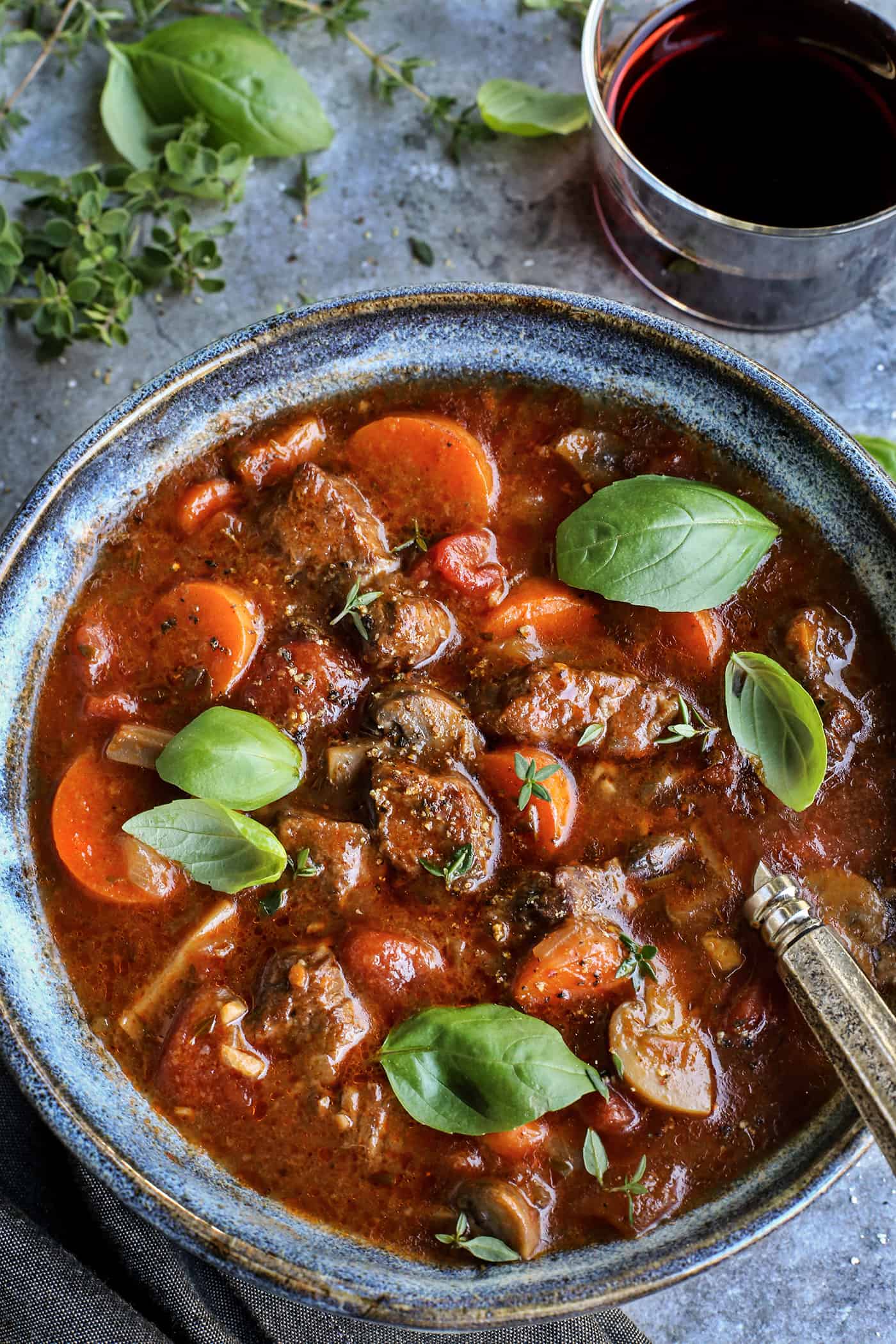 beef stew in a blue bowl, with a glass of red wine