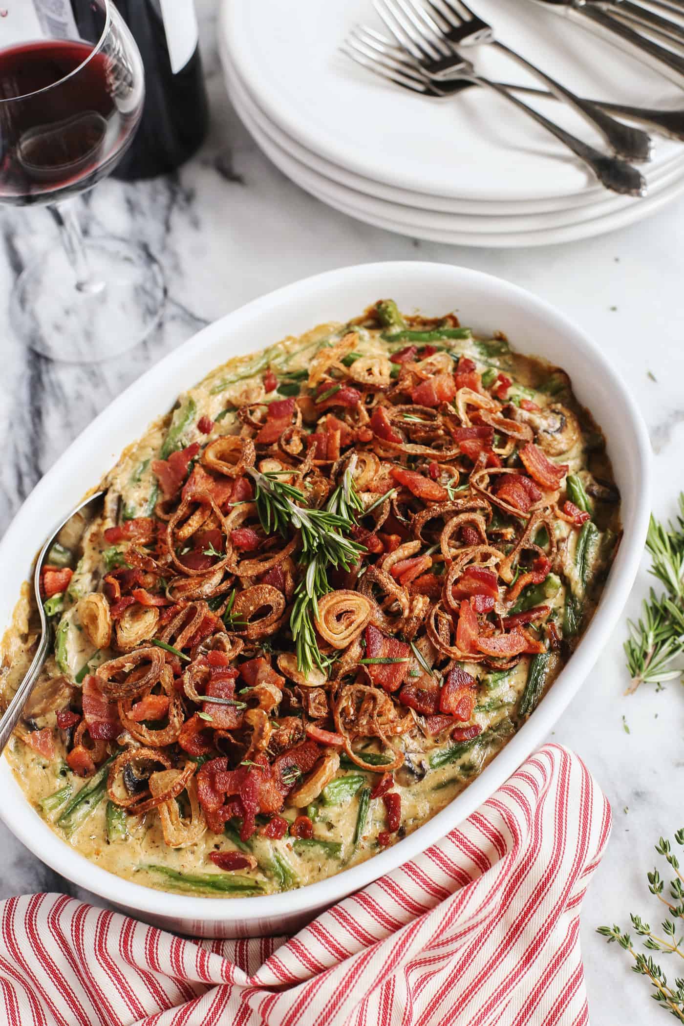 This from-scratch Green Bean Casserole features fresh green beans, crispy bacon, fried shallots, and a creamy homemade gravy. Green bean casserole with bacon and crispy fried shallots in a white serving dish.