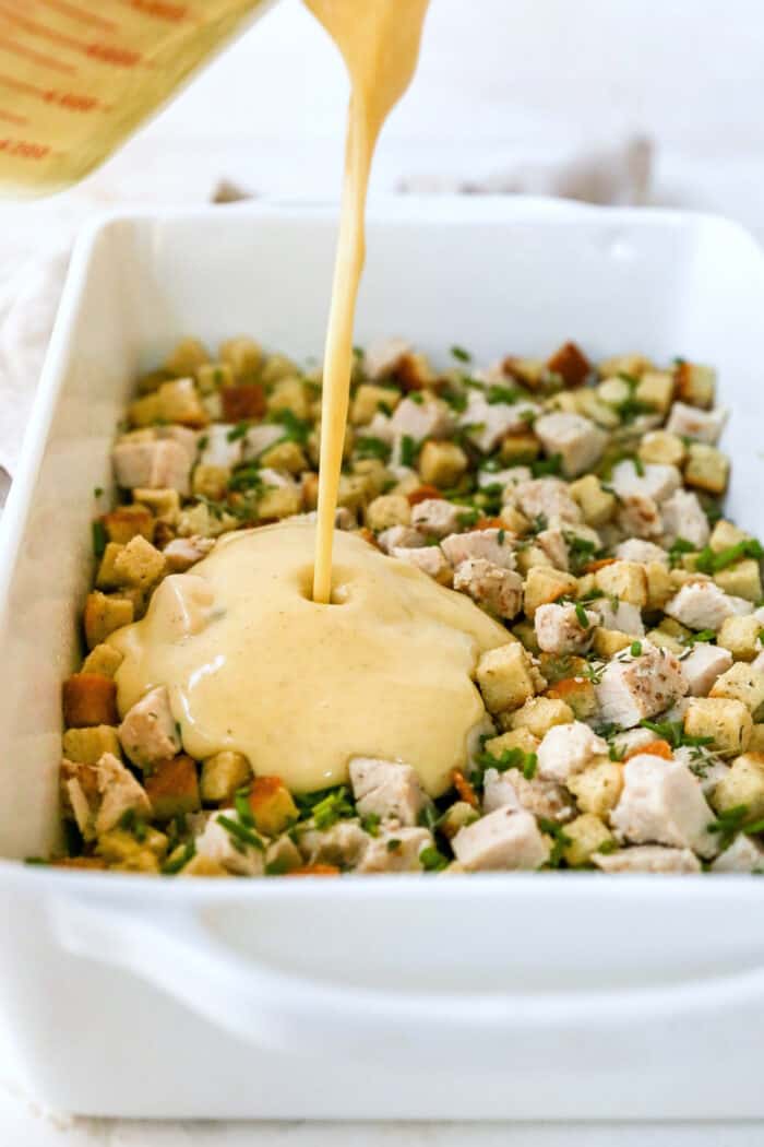 Pouring creamy sauce over turkey and stuffing mixture in white serving dish