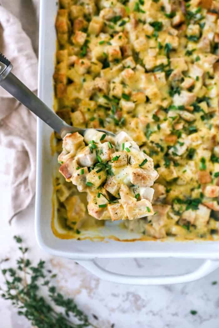 white rectangular serving dish of leftover turkey casserole, with a big spoon lifting out of it