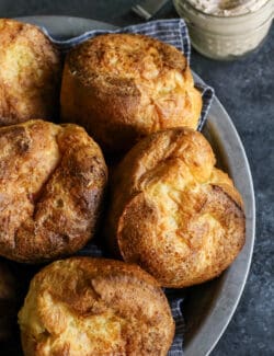 baked popovers in a metal plate, with a jar of cinnamon honey butter on the side