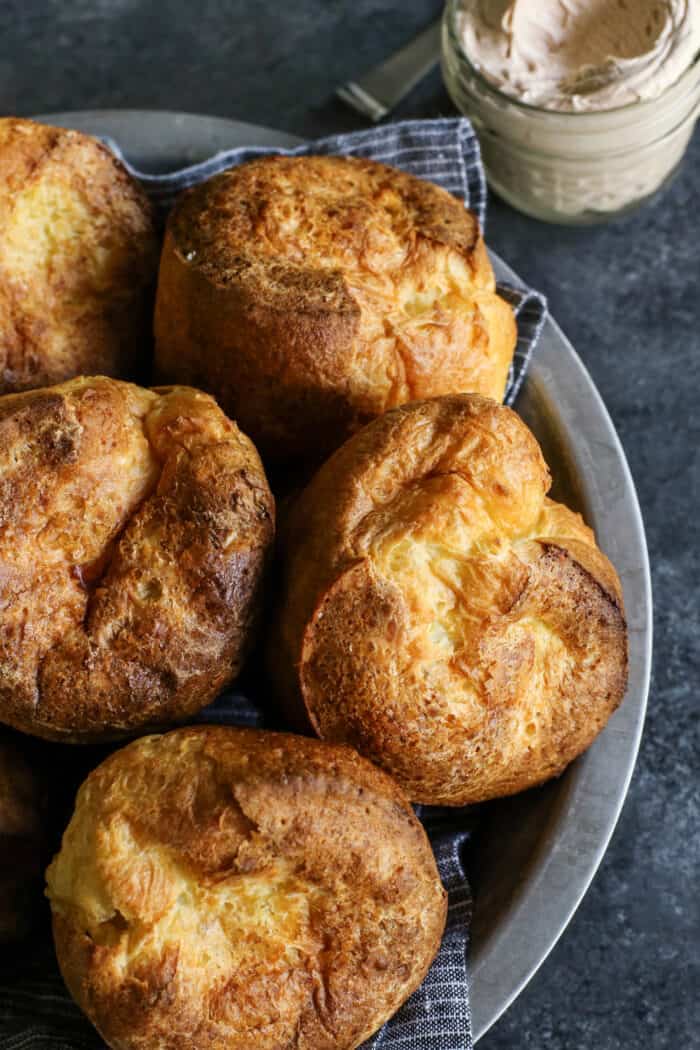 baked popovers in a metal plate, with a jar of cinnamon honey butter on the side