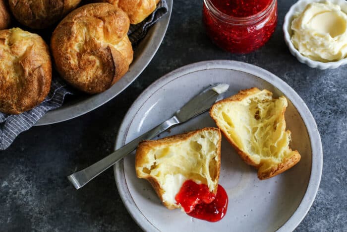 a popover split open on a plate, with butter and jam