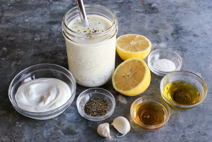 a jar of lemon yogurt dressing, plus yogurt, cut lemon halves, garlic, olive oil, honey, salt and pepper