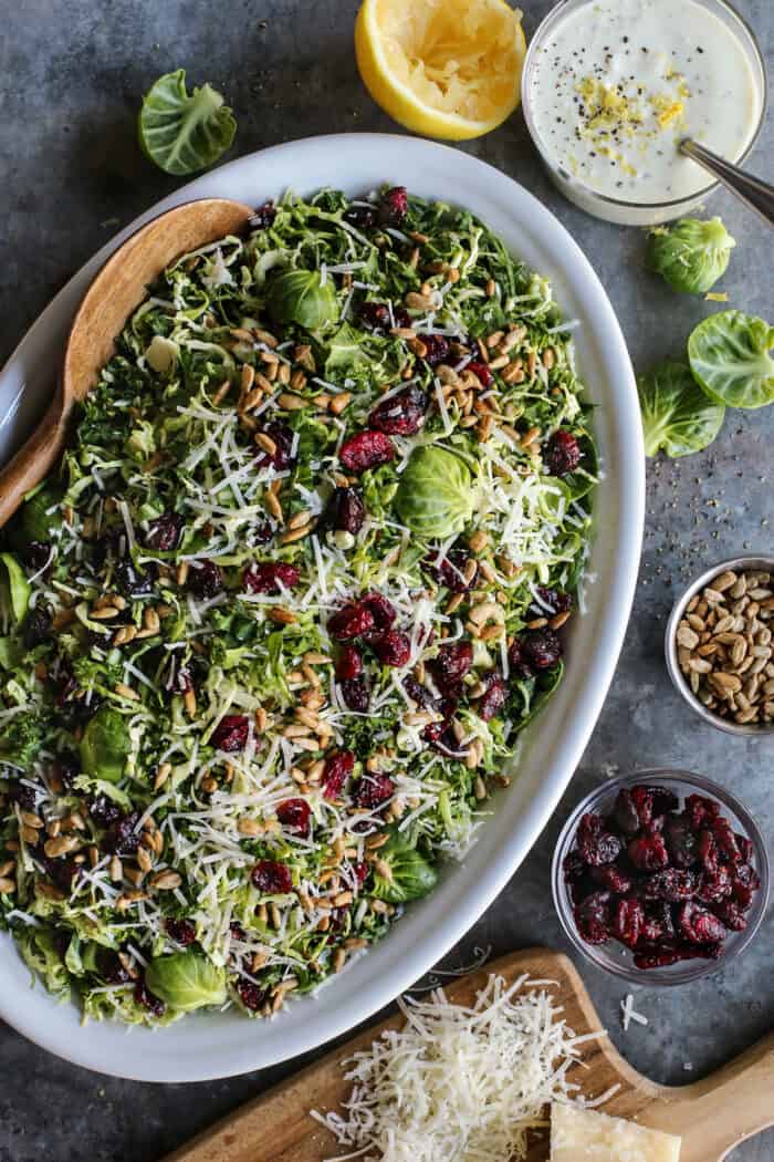 shaved Brusssels sprouts salad on an oval white platter with a jar of lemon yogurt dressing