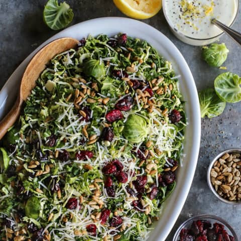 shaved Brusssels sprouts salad on an oval white platter with a jar of lemon yogurt dressing