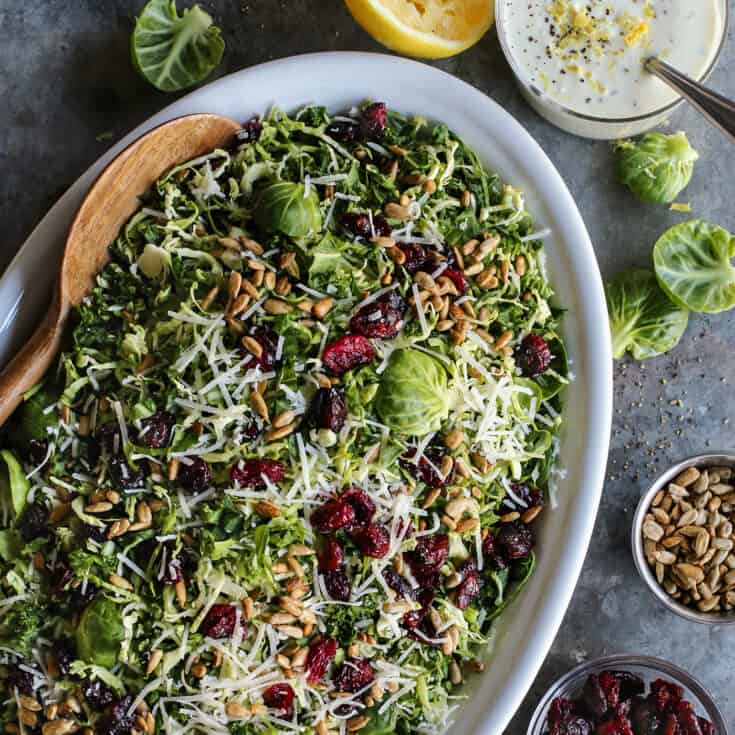 shaved Brusssels sprouts salad on an oval white platter with a jar of lemon yogurt dressing