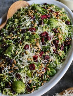 Salad of shaved Brusssels sprouts on an oval white platter with a jar of lemon yogurt dressing.