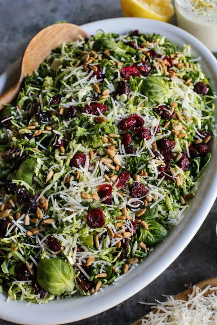 salad of shaved Brusssels sprouts on an oval white platter with a jar of lemon yogurt dressing