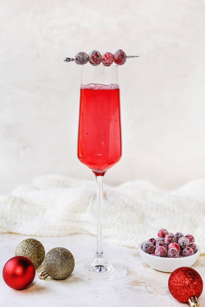 a champagne flute filled with a cranberry cocktail, garnished with a swizzle stick of sugared cranberries