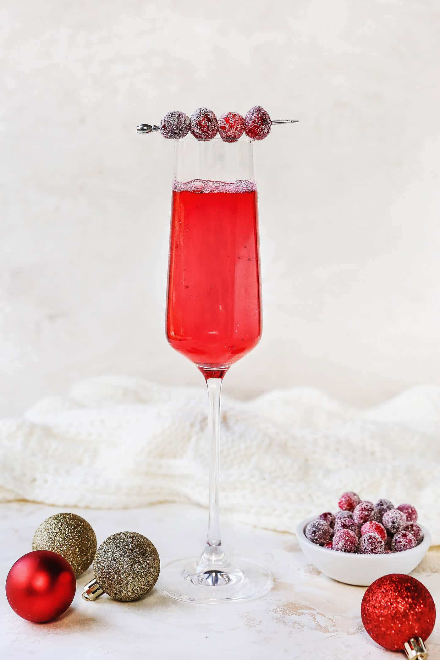 A champagne flute filled with a cranberry cocktail, garnished with a swizzle stick of sugared cranberries.