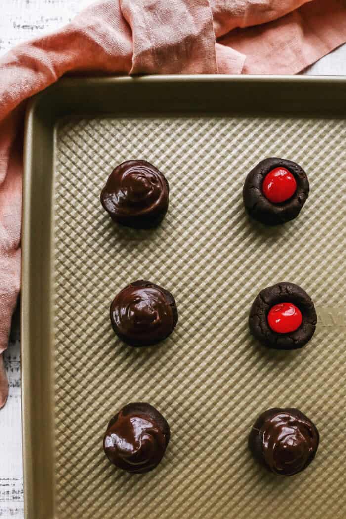 balls of chocolate cookie dough with a cherry in the middle and chocolate frosting covering the cherry