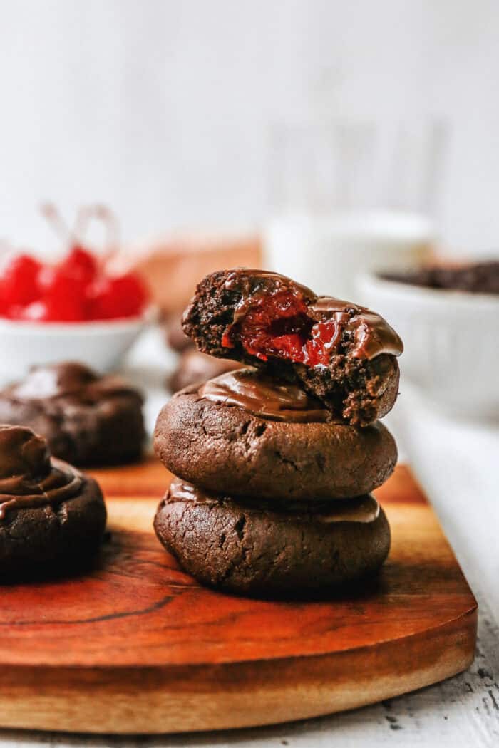 a stack of chocolate cherry cookies, one has a bite to show the cherry inside