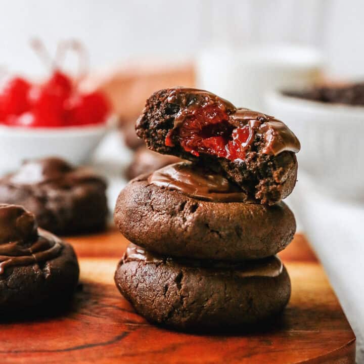 a stack of chocolate cherry cookies, one has a bite to show the cherry inside