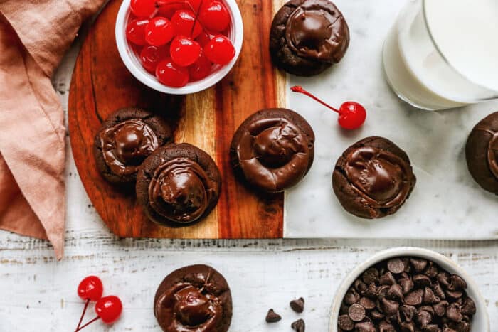 overhead photo of chocolate covered cherries on a wood and marble board with a glass of milk and bowl of cherries