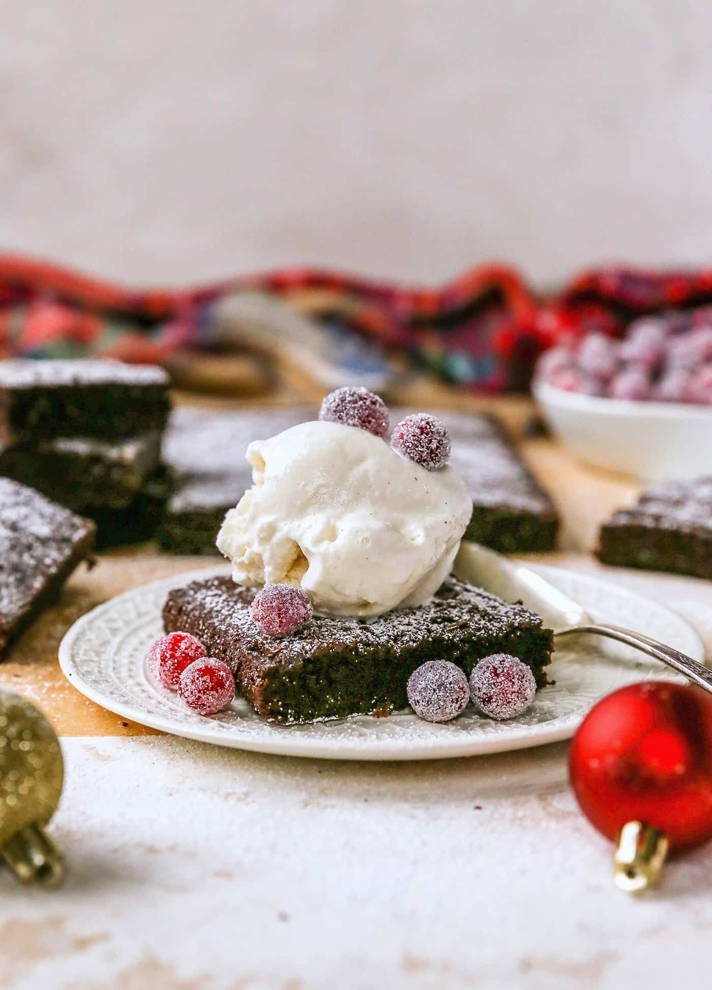 a gingerbread brownie on a plate with sugared cranberries and a scoop of ice cream