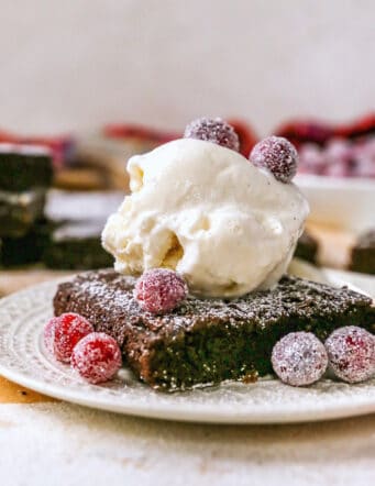 a gingerbread brownie on a plate with ice cream and sugared cranberries