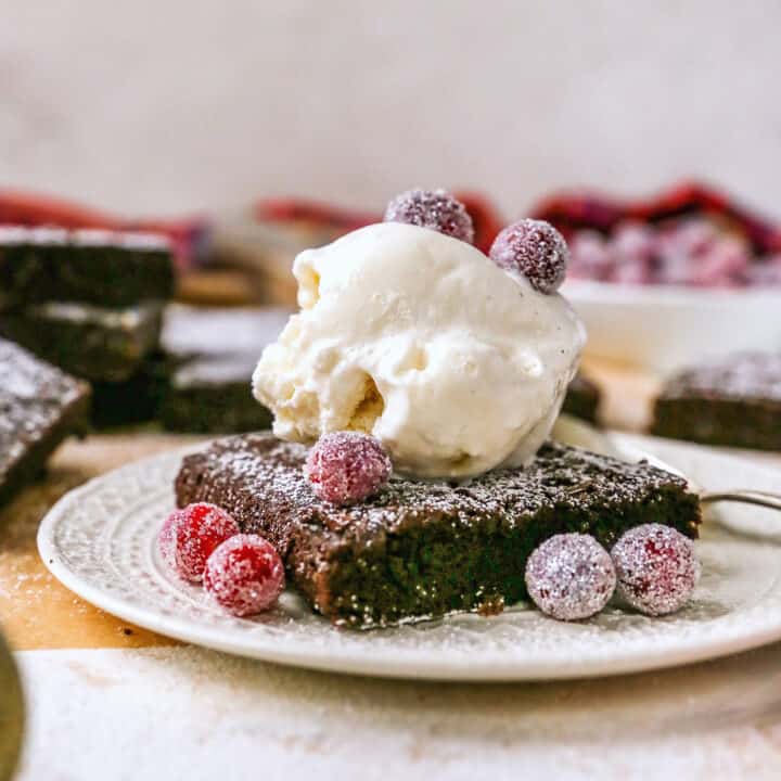 a gingerbread brownie on a plate with ice cream and sugared cranberries