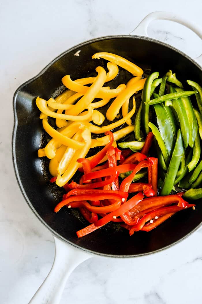 strips of raw colorful bell peppers in a white skillet