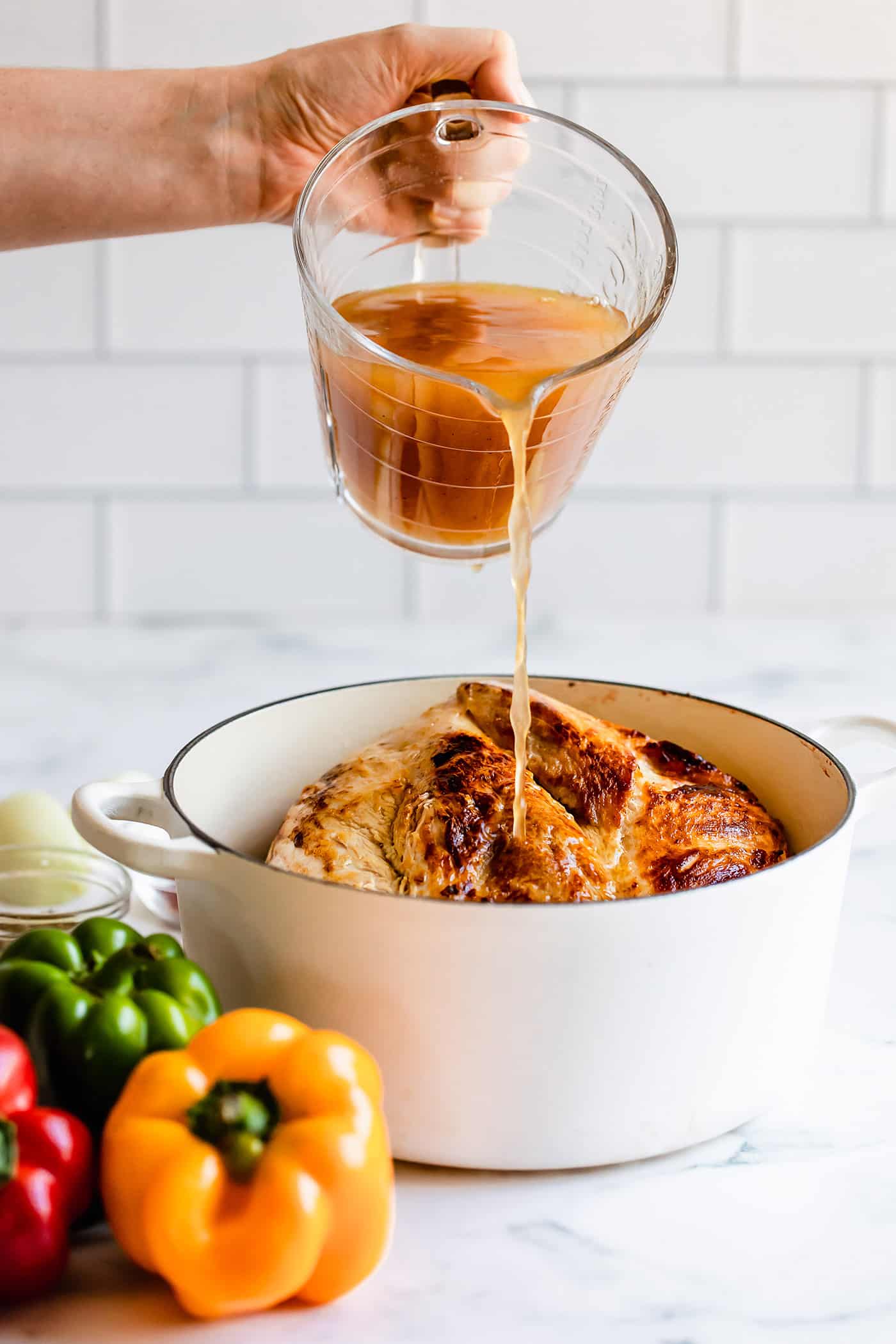 pouring chicken broth into pot with seared pork shoulder