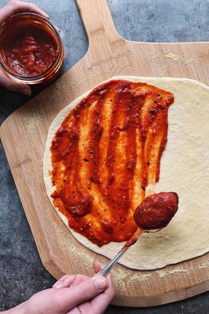 spooning red sauce onto pizza dough