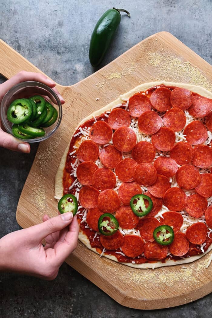placing jalapeno slices onto pepperoni pizza
