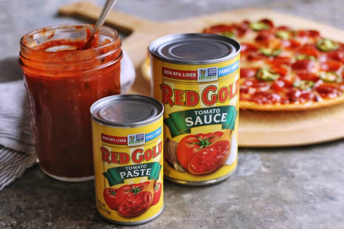 cans of tomato sauce and paste, jar of homemade pizza sauce, and a homemade thin crust pizza